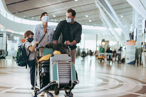 Family walking at airport with luggage trolley