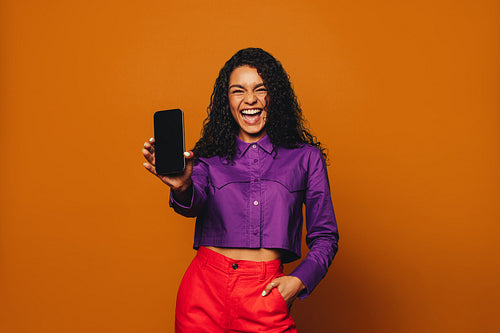 Cheerful woman recommending vibrant colours with her mobile device on orange background