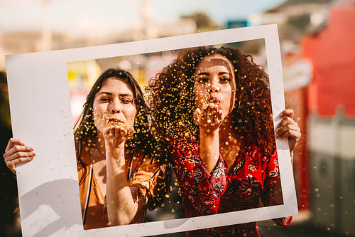 Beautiful friends blowing glitter through empty photo frame