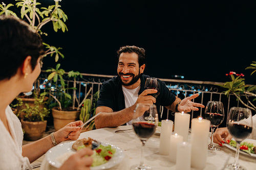 Friends enjoying dinner outdoors with wine and candles