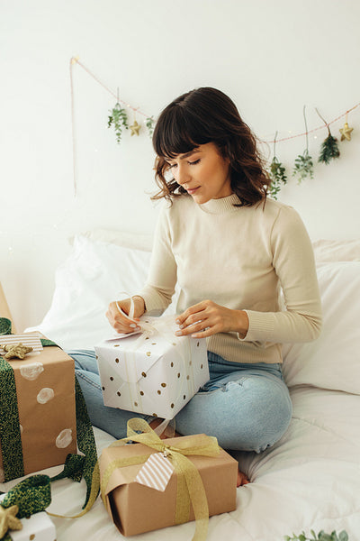 Woman packing christmas presents sitting on bed