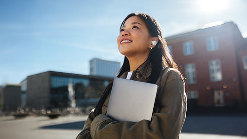 Young female student commuting to university smiles while holding laptop
