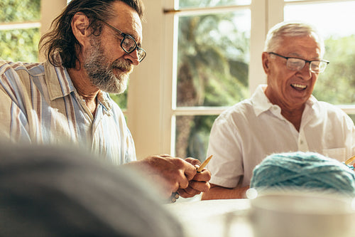 Senior beard man knitting with friend sitting by