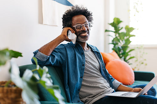 Mature man enjoying remote work from home, talking on a smartphone on a couch