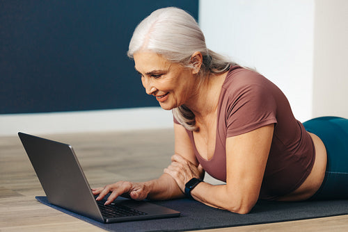 Yoga community: Woman connecting with other yogis online while using her laptop on the mat