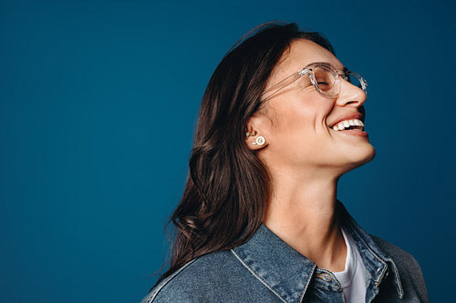Laughing woman in glasses and denim jacket against blue background