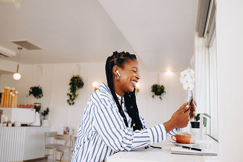 Cheerful young businesswoman having a video call on a smartphone while working in a coffee shop