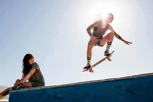 Woman skateboarding at park with friend sitting on ramp