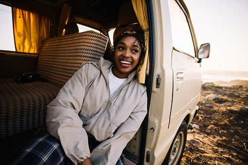 Smiling traveler sits in a van by the coast at sunset