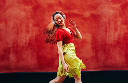 Woman dances with headphones outdoors against a vibrant red wall