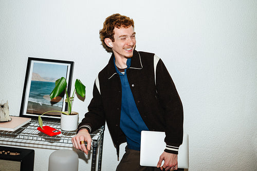 A productivity-focused work portrait shows a young man holding a laptop at home.