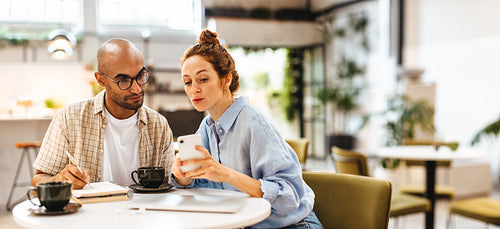 Business woman showing her client her mobile phone while discussing work
