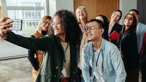 Diverse group of successful coworkers taking a joyful selfie at work during a daytime event in a modern office setting