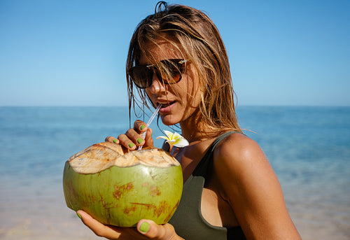Attractive woman drinking coconut water on the beach