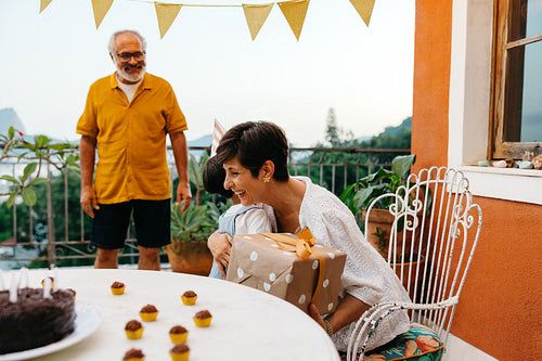 Family celebrating a birthday on a terrace with presents and cake