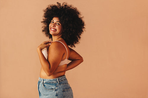 Body confident young woman smiling happily while wearing a bra and jeans