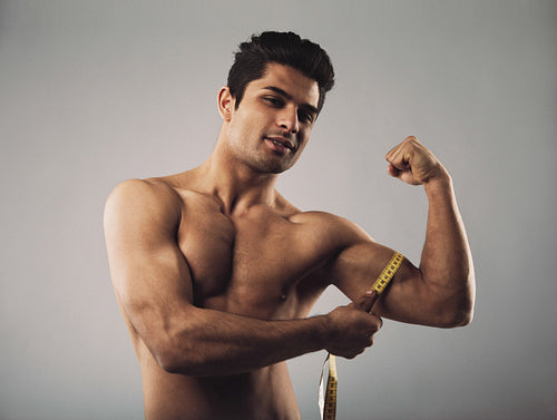 Masculine young male measuring biceps with tape measure