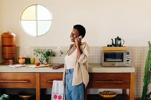 Happy Afro-Brazilian woman talking on mobile phone in kitchen