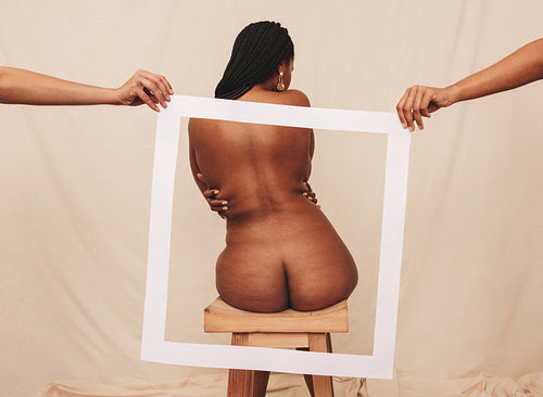 Rearview of a young woman sitting nude behind a picture frame