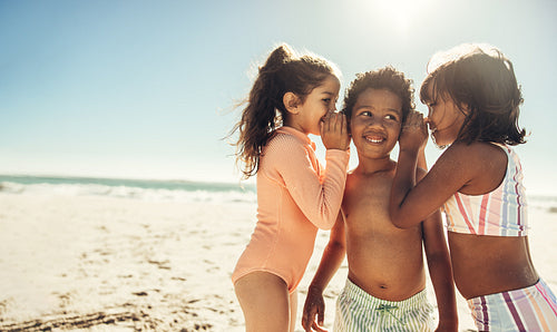 Two playful girls whispering to their friend at the beach
