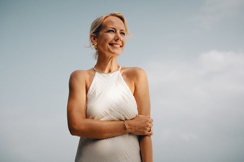 Elegant mature woman posing confidently against a serene blue sky backdrop