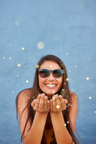 Young woman blowing confetti in the air and smiling