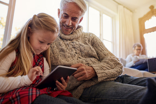 Senior man with granddaughter using digital tablet at home 