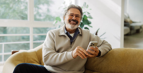 Senior man uses smartphone while relaxing at home