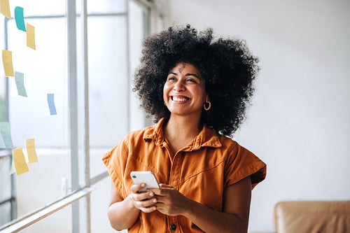 Pensive businesswoman holding a smartphone in a creative office