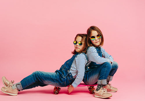 Stylish twin girls sitting together on a skateboard