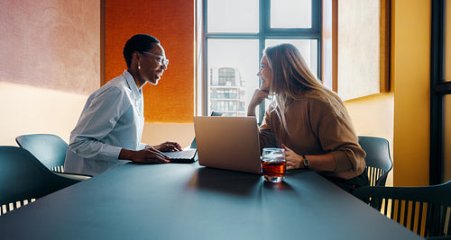 Two women in a modern office sharing ideas at a table with laptops