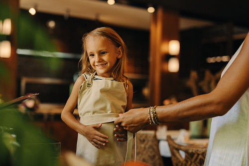 Child smiling while wearing an apron in a warm indoor setting