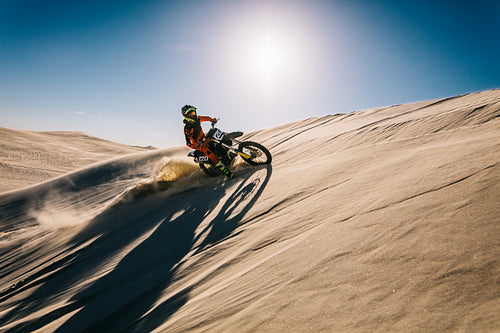 Professional motocross biker riding across sand dunes