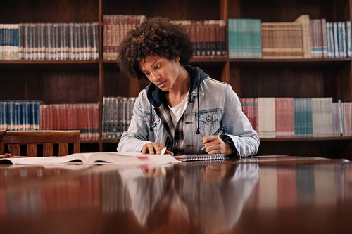 Young student making notes from books in library