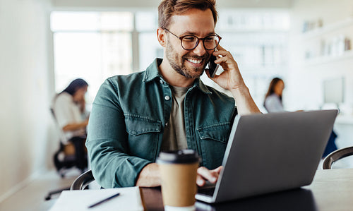 Male software designer speaking to a client on the phone in an office