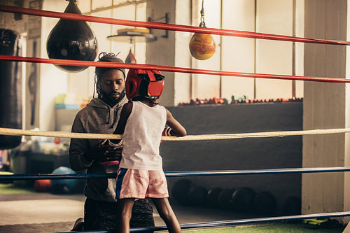 Boxing kid standing inside the ring talking to his trainer. 