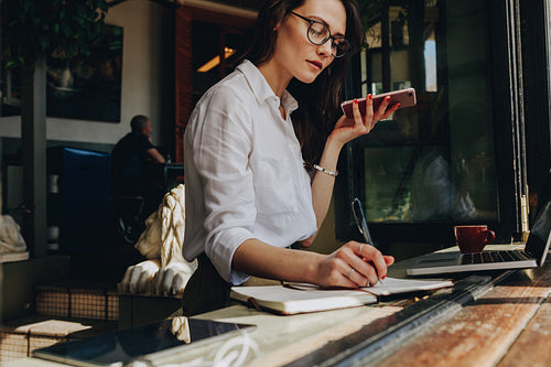 Businesswoman talking on phone and making notes at cafe