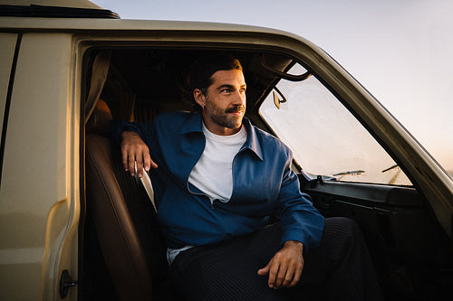 Man sitting in van looking out at sunset during travel