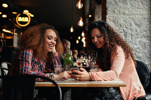 Young women sitting at cafe and using phone
