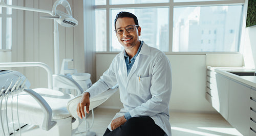 Dentist sits beside a dental chair in a modern clinic portrait