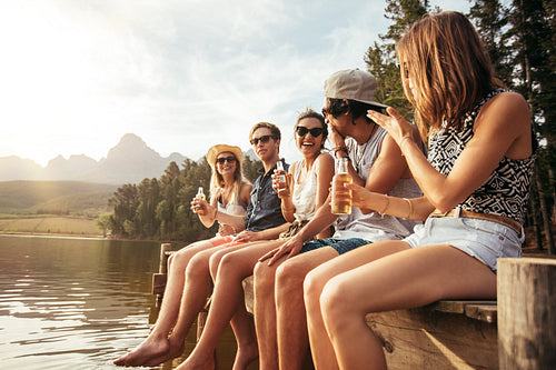 Friends sitting on pier at lake drinking beers