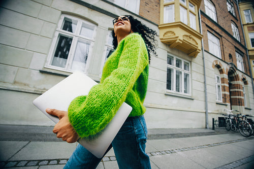 On a sunny commute, the woman carries a laptop through the city for work