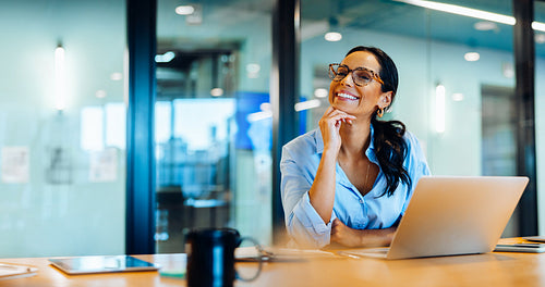 Smiling woman wearing glasses working at a desk with a laptop