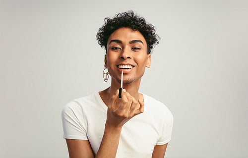 Androgynous man putting on lip gloss