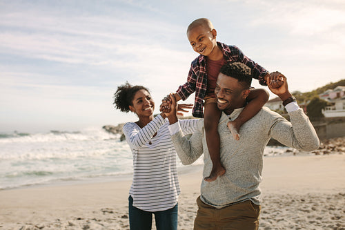 Parents carrying son on shoulders on beach vacation