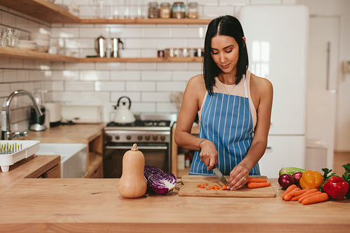 Young woman cutting vegetables in kitchen at home