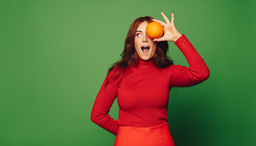 Cheerful woman holding a fresh orange on green background