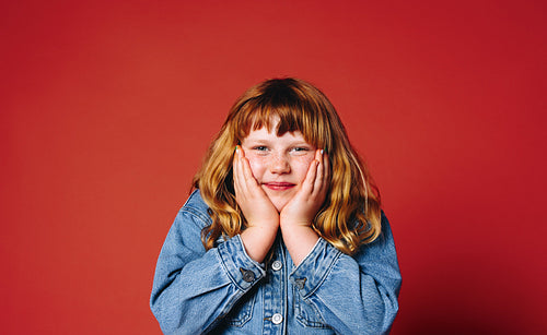 A young girl portrait in denim jacket posing with hands on face in studio