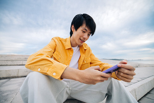 Young man in outdoor setting smiling while using smartphone