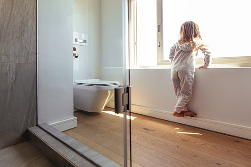 Little girl looking outside a bathroom window